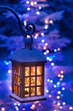 Bokeh arka planına karşı fener, Noel ışıkları ve karlı ağaçla