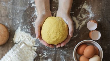 Hamuru yoğurmak. Kadın eli ev yapımı hamuru tutar. Masanın üzerinde un, peçete, yumurta ve kabuklar var.