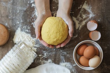 Hamuru yoğurmak. Kadın eli ev yapımı hamuru tutar. Masanın üzerinde un, peçete, yumurta ve kabuklar var.