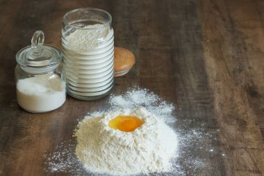 Hamuru yoğurmak. Masanın üzerinde un ve ortasında bir yumurta var. Cam kavanozlarda un ve tuz depolamak için..