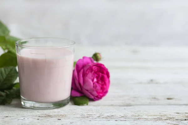 Аюрведический напиток розовое молоко или маття. Стакан освежающего коктейля стоит на деревянном белом фоне. Рядом находится лиловая роза. — стоковое фото