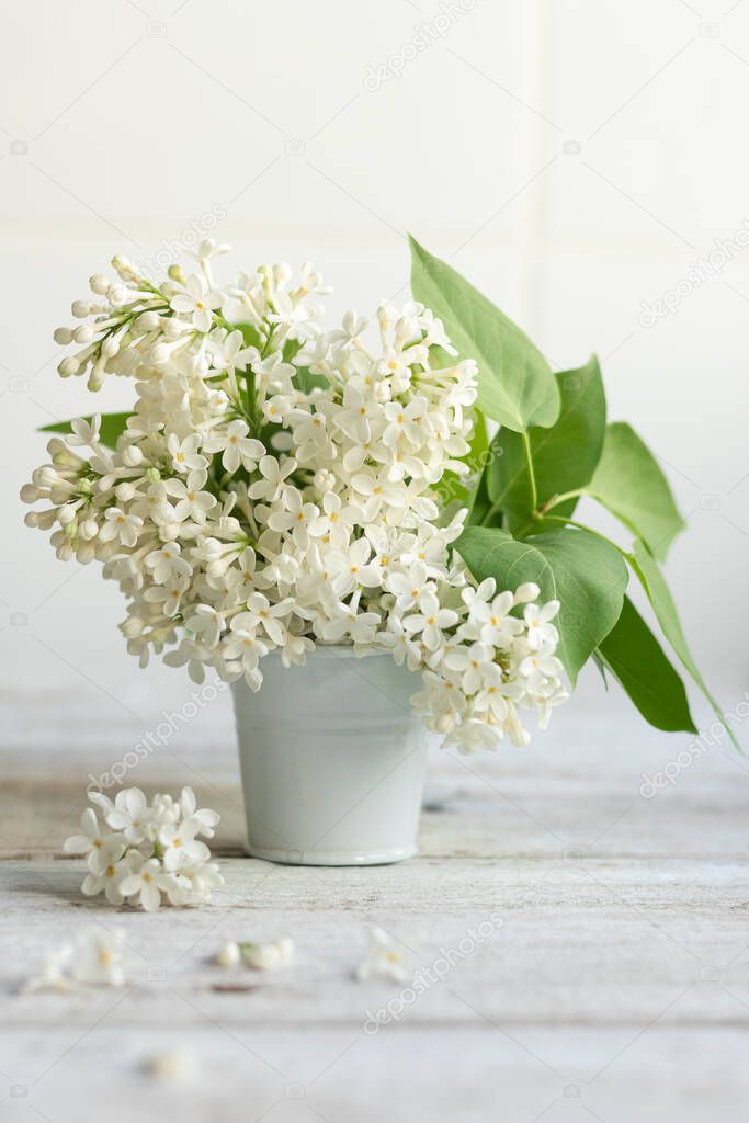 Bouquet of white spring flowers of lilac in a ceramic vase on a light wooden background. Festive interior decoration. Soft focus.