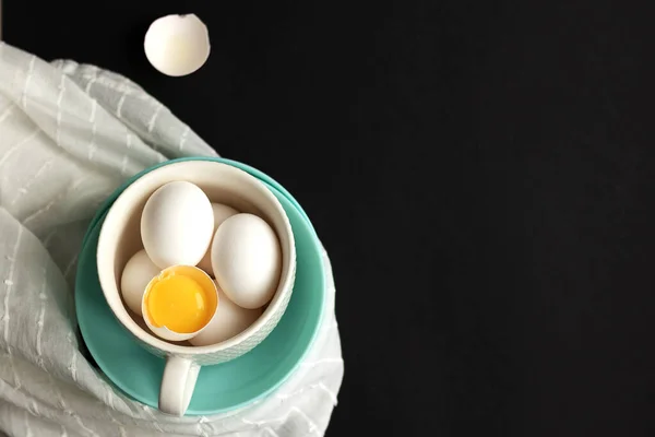 Traditional easter eggs. One egg is broken and the yolk is visible. Colored dishes on a wooden table and black background. Minimalistic design. White napkin and eggshell.