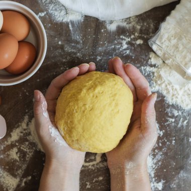 Hamuru yoğurmak. Kadın eli ev yapımı hamuru tutar. Masanın üzerinde un, peçete, yumurta ve kabuklar var.