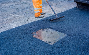 İşçi yoldaki bir tümseği onarmak için yeni asfalt döşemeyi düzenler.