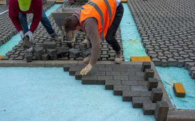 Paving taş işçisi bir şehir caddesinin inşaatı sırasında kaldırımları örülmemiş kumun üzerine yerleştiriyor ve yerine yerleştiriyor..