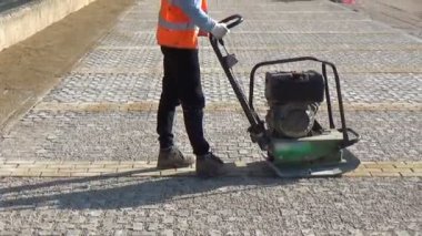 İşçiler, yatakları içindeki blokları sıkıştırmak için vibro-sıkıştırıcı plaka kullanıyorlar.