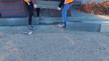 Kaldırım inşaatında beton kaldırım taşı döşeyen ve metal kazıklı sicimler kullanan işçiler.