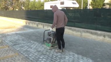 İşçiler, yatakları içindeki blokları sıkıştırmak için vibro-sıkıştırıcı plaka kullanıyorlar.