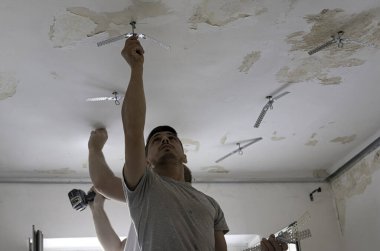 İnşaat işçisi asılmış tavanı bir alçıpanla monte ediyor. D, alçıpanı tornavidayla tavandaki metal çerçeveye yerleştiriyor.