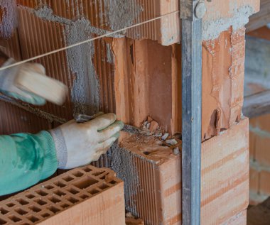 Çekiç ve keskiyle tuğla ustası, duvarda başka bir duvarı aşılamak için delik açar. 