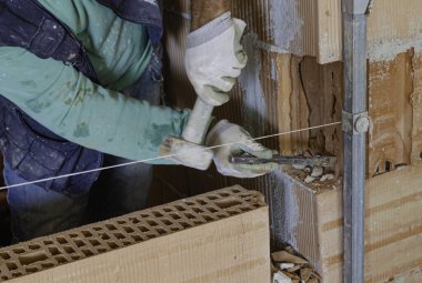 Çekiç ve keskiyle tuğla ustası, duvarda başka bir duvarı aşılamak için delik açar. 