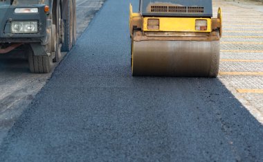 İşçi, asfaltı sıkıştırmak için titreşen yol silindirine önderlik eder. Yol yapımı için hazırlanır, Seçici Odaklanma