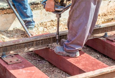 Ahşap yataklı demiryolu inşaatı. Matkapla çalışan işçi, korkuluğu sabit tutan sürgüyü onaracak deliği yapar..
