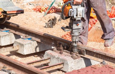 Ahşap yataklı demiryolu inşaatı. İşçi özel bir aletle korkuluğu betona bağlayan cıvata vidalıyor