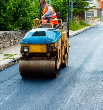 Asfalt kaldırımda hafif titreşimli paten sıkıştırıcı işçisi yol onarımı için çalışır