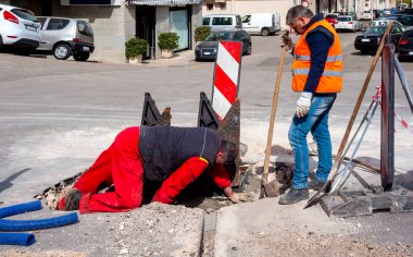 İşçiler, optik fiberlerin yeni ağ altyapısının çalışması için kokpiti dökme demir rögar kapağıyla üçgen kanatlara kapatırlar.