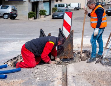 İşçiler, optik fiberlerin yeni ağ altyapısının çalışması için kokpiti dökme demir rögar kapağıyla üçgen kanatlara kapatırlar.
