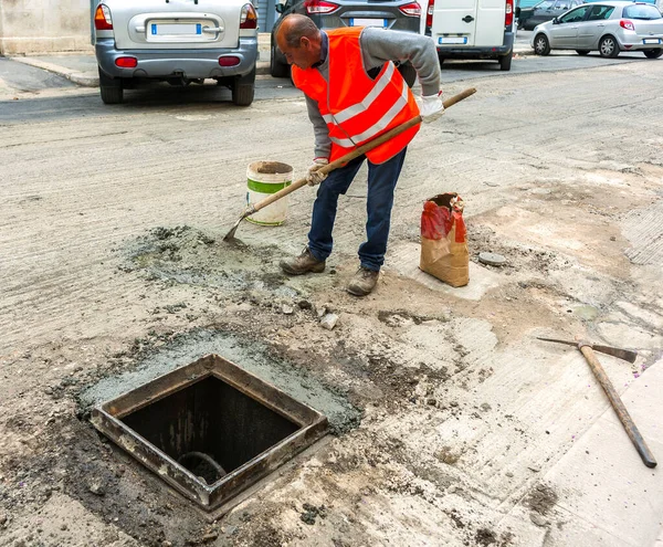 工人用快速凝固的水泥准备砂浆 以固定城市下水道检查井的铸铁井盖 — 图库照片