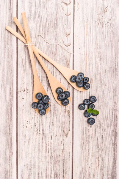 Fresh blueberries with wooden spoon and mint leaf on rustic text — Stock Photo, Image