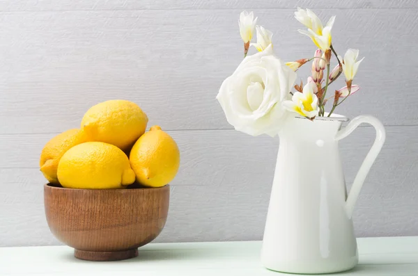 Träskål med citroner och vita blommor i kannan. Rosor i kruka. — Stockfoto