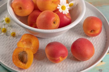 Tahta masadaki bir kasede lezzetli olgun kayısılar. Kayısılar ve papatya çiçekleriyle yakın plan.