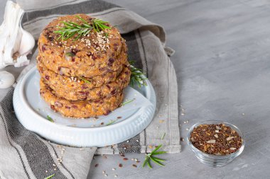 Çiğ vejetaryen burger, kinoalı, kırmızı tavuk, sebze ve biberiye yapraklı mutfak tezgahı.
