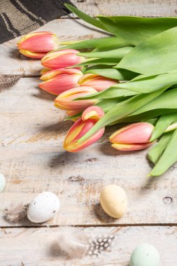 Paskalya yumurtaları ve çiçek açan laleler. Üst katman düz. Parlak pembe ve sarı lale bahar çiçeği. Paskalya kompozisyonu renkli Paskalya yumurtaları ve bahar çiçekli laleler ahşap arka planda. Paskalya kartı kopyalama alanı.