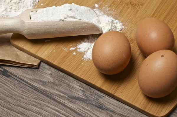 Flour spoon and eggs on wooden table. — Stock Photo, Image