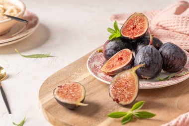 Tabakta bütün ve dilimlenmiş incir yığını ve stevia yapraklı ahşap bir tahta, pembe bir peçete ve kırsal alanda bir kase.