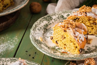 Yeşil çiçekli bir tabakta yeşil fındıklı ekmek diliminin yakın plan resmi. Üstünde şeker, badem, ceviz ve Noel süsleri olan yeşil bir masa. Bolo Rainha, Portekiz Noel tatlısı..