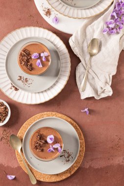 An overhead view of two delicious chocolate mousses in glasses, styled on plates with spoons and garnishes, a sweet presentation.