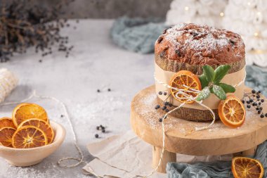 Kurumuş portakal ve çobanpüskülü ile süslenmiş şeker tozlu panet tonu, Noel temalı bir ortamda kurutulmuş portakal kasesinin yanındaki ahşap tezgahta.