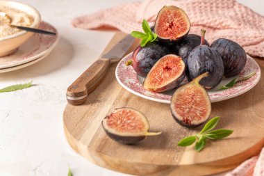 Olgunlaşmış ve dilimlenmiş incirler bir tabakta ve bir bıçakla ahşap bir tahta ve bir kase parçalanmış kırsal bir yerde.