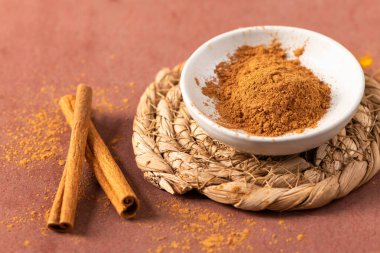 Yemek pişirme ve yemek pişirme temaları için ideal dokulu, kırmızımsı kahverengi bir arka plana karşı tarçınlı aromatik zemin tarçın ve kırsal örülmüş bir altlık üzerindeki tüm ovalar içeren topraksı bir yemek fotoğrafı kompozisyonu.