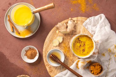 Seramik bir fincanda seramik bir latte ve yanında taze zencefil kökü ballı tarçın ve kırsal bir masanın üstüne serpiştirilmiş baharatlar.