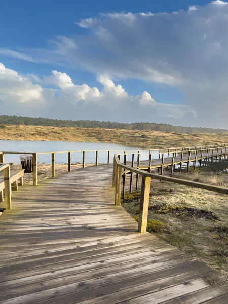 Ovar Portekiz 'de Furadouro plajı yakınlarındaki dinamik, bulutlu bir gökyüzü altında, sakin bir lagünün yanında, bataklık zeminine uzanan ahşap bir sahil yolu, doğal ve sakin bir kıyı manzarası sunar.