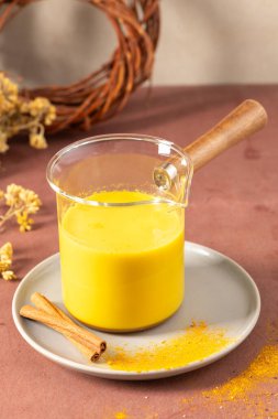 Profesyonel bir hayat tarzı. İçinde parlak sarı zerdeçal latte, cam sürahinin içinde. Tarçın çubukları ve pudra dolu bir fincan altlığının üzerinde ahşap sapı var.