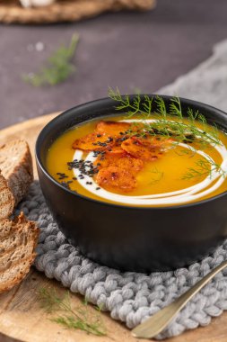 Koyu bir kase kremalı havuç çorbası, beyaz kremalı siyah susam tohumu ve haşlanmış havuç dilimleri, ekşi ekmek ve pirinç kaşık.