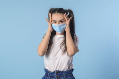 Tıbbi maske takan genç bir kız. Coronavirus önleme koruma grip soğuk yüz maskesi mavi pastel arka plan üzerinde