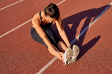 Kız stadyumdaki koşu bandında oturuyor.