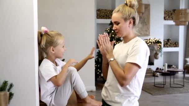 Ung blond mamma med en liten dotter i ett dekorerat nyårshus leker med händerna — Stockvideo
