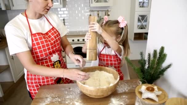 Una giovane madre bionda con una piccola figlia in grembiuli è impegnata a cucinare a tavola in cucina.. — Video Stock