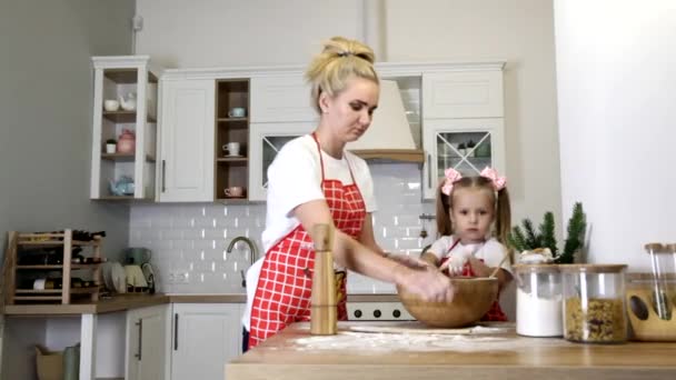 A young blonde mother with a small daughter in aprons are engaged in cooking at the table in the kitchen. — Stock Video