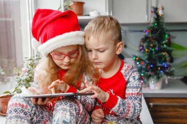  Erkek ve kız kardeşler mutfakta Noel Baba şapkalarıyla oturup yastığa bakarlar. Çocuklar Noel Baba 'ya mektup yazar.