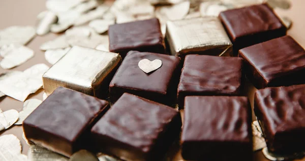 Eingewickelte und ausgepackte quadratische Schokoladenbonbons zwischen den in Folie geschnittenen Herzen in Großaufnahme. Das Konzept des Valentinstages — Stockfoto