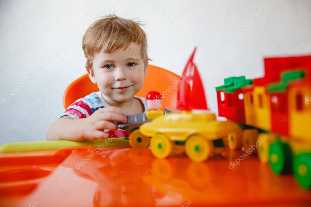 A small blond boy at home sitting at an orange children's table playing a colorful plastic construction kit. High quality photo