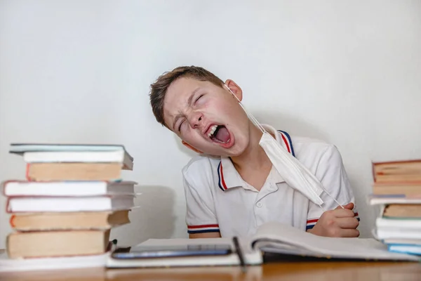 Teenager at home for textbooks pulls off his mask with a grimace of relief. High quality photo