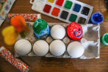 Madalyalı ve bir büfede beyaz yumurtalar, masaya boya ve süslemeler. Üst Manzara. Paskalya için hazırlanılıyor