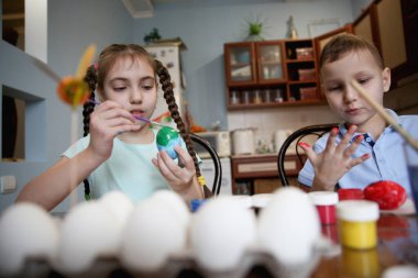 Esmer erkek ve kız kardeş evdeki masada oturan Paskalya yumurtalarını süslerler. Yüksek kalite fotoğraf